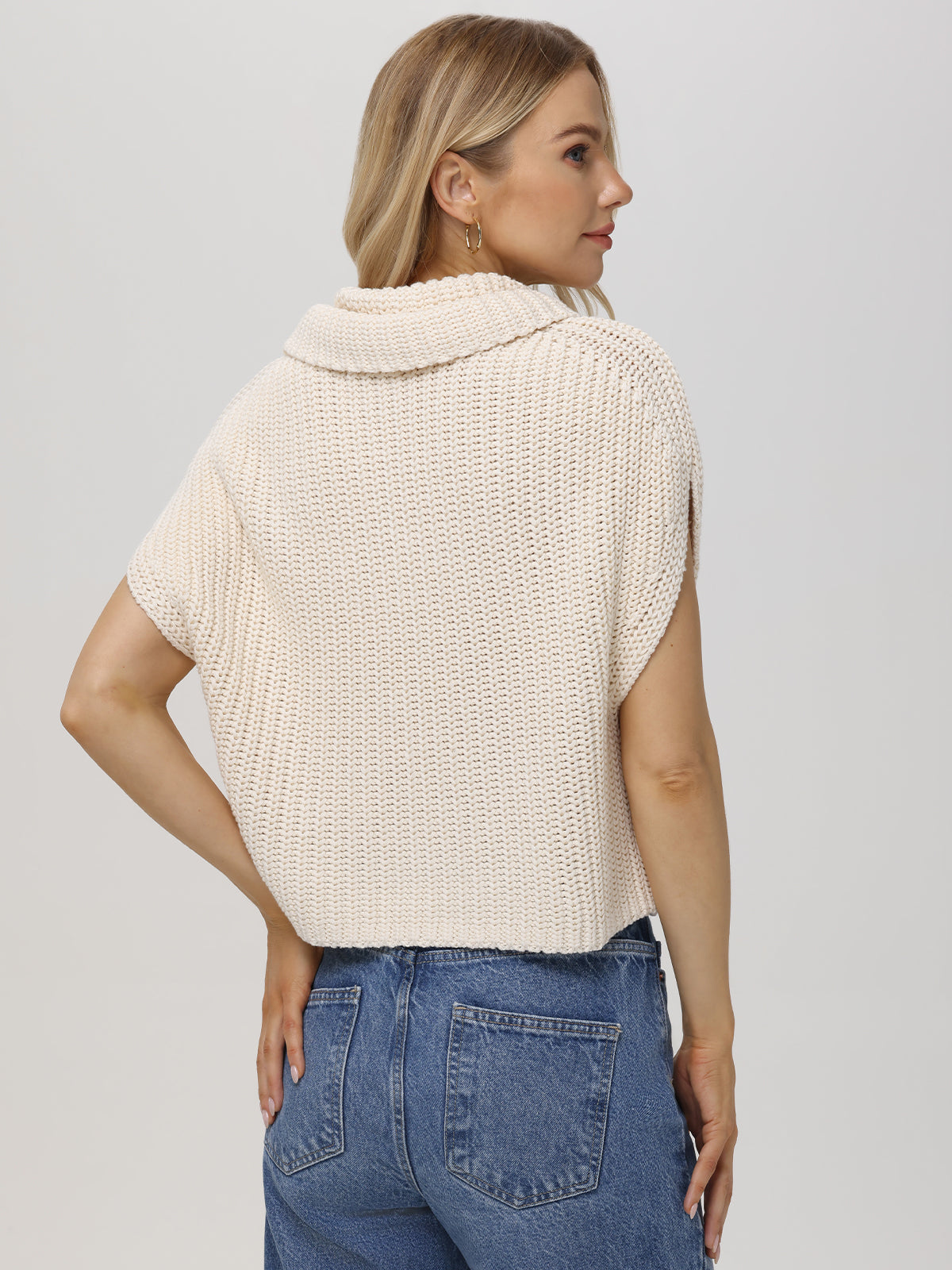 A woman with blond hair is seen from behind wearing a 100% cotton cream-colored sweater by 525 America. It features a wide chunky neck and short sleeves, perfectly paired with her blue jeans against a plain, light-colored background.