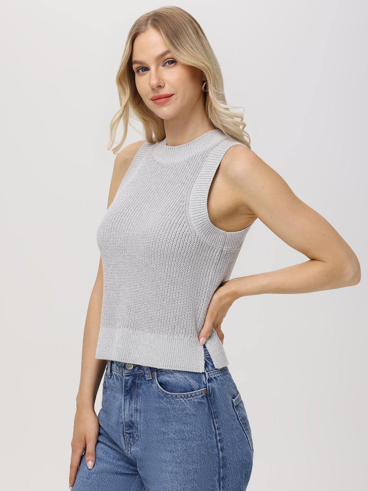 A woman with long blonde hair wears a gray, fitted-length knit top by 525 America and blue jeans. In a slight side profile facing the camera against a plain light background, her ensemble subtly hints at a dazzling outfit.