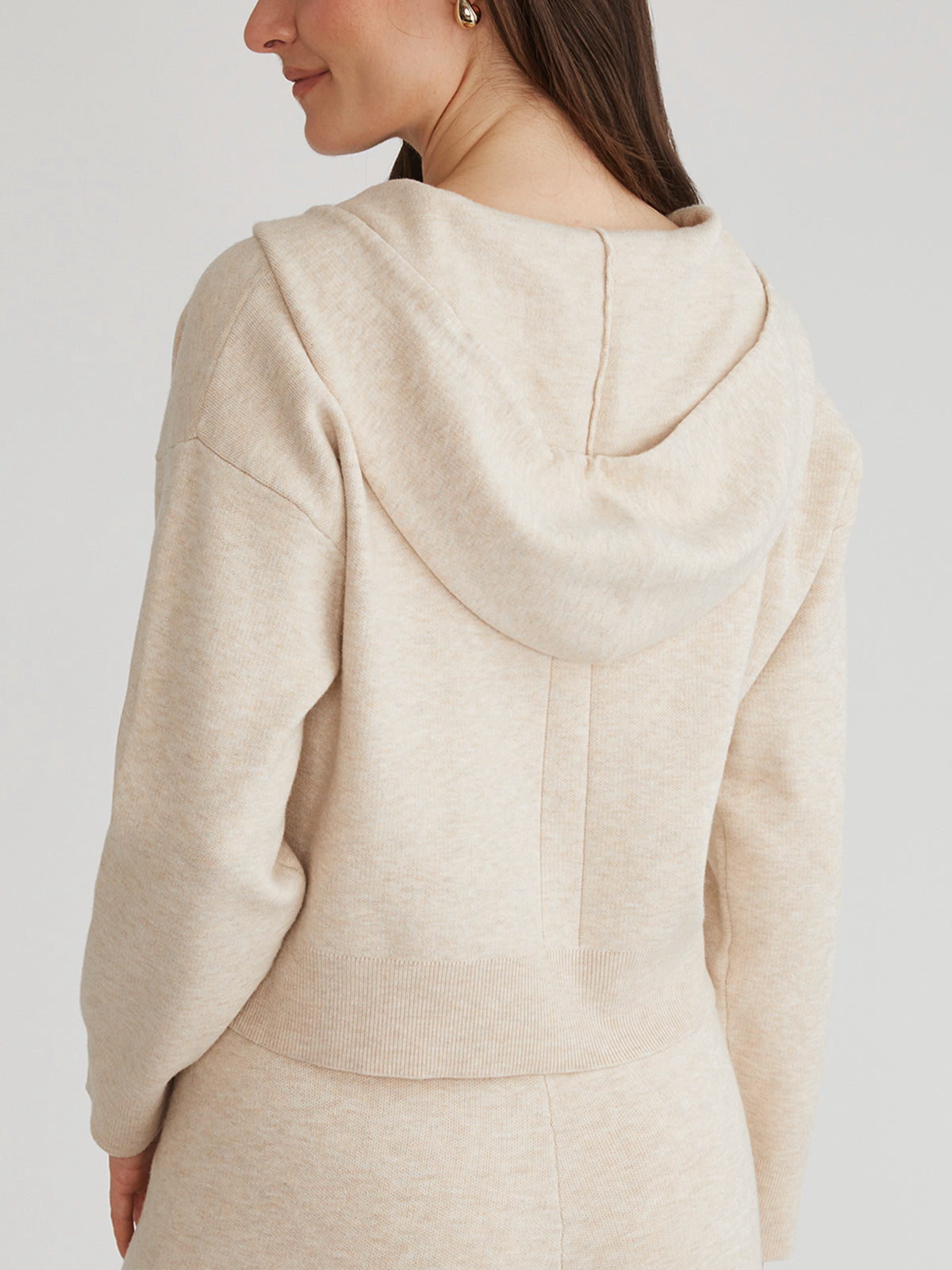 A person with long hair is seen from the side wearing a cozy hooded light beige hoodie by 525 America, which features a relaxed fit and ribbed hem against a neutral background.