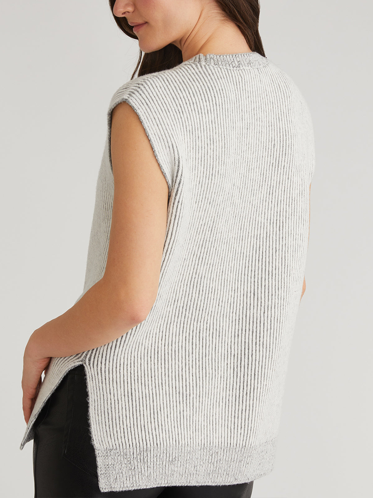 A person with long dark hair wears the 525 America Jasmine Contrast Rib Vest, a loose-fitting sleeveless light gray knit top. Paired with black pants, they stand against a plain background, turned slightly to the side—making a fashion-forward wardrobe choice.