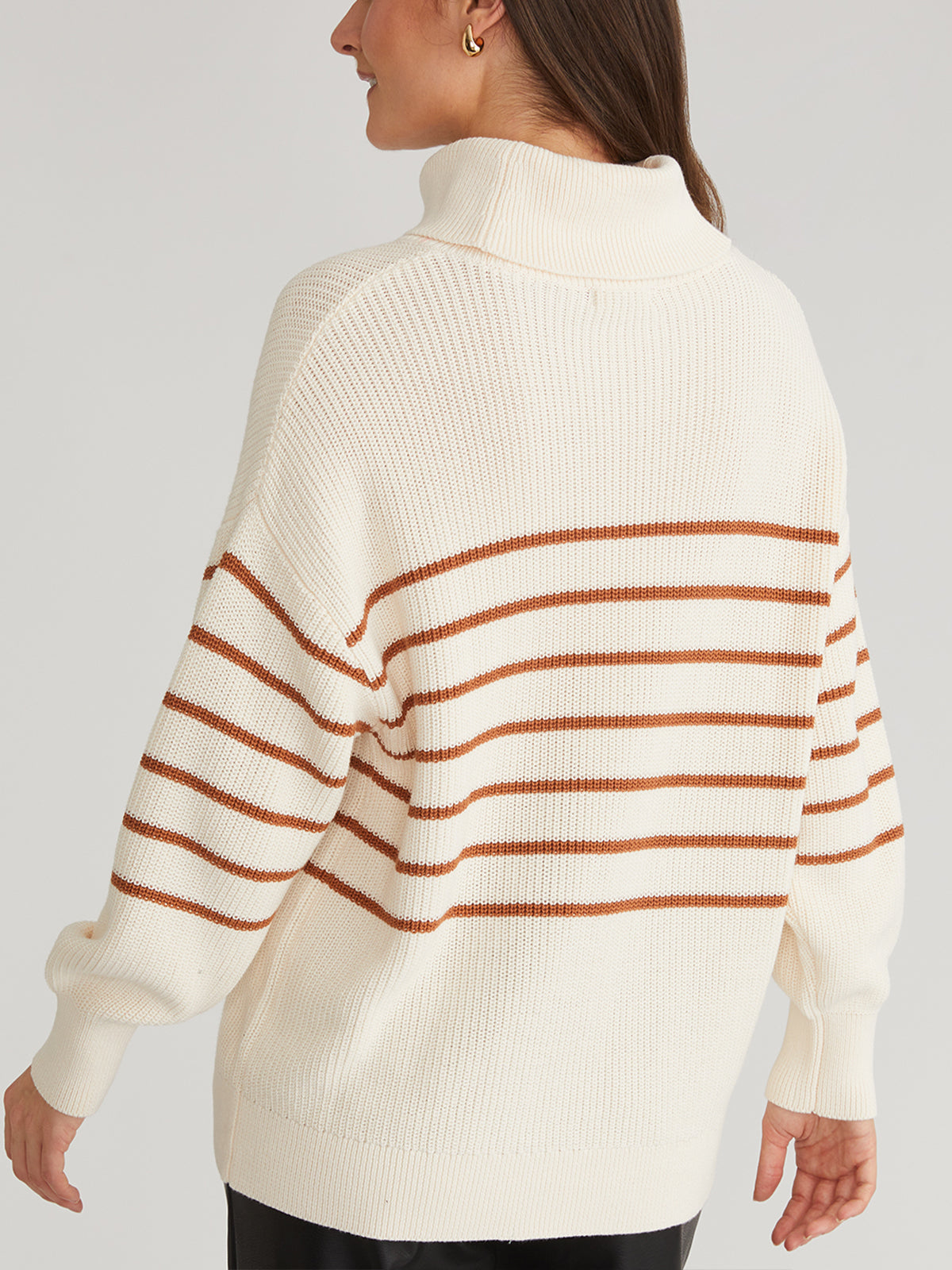 A person with long brown hair wears a 525 America oversize stripe turtleneck made from 100% cotton. Facing away from the camera, they highlight the pullover sweaters chic design against a plain, light-colored background.