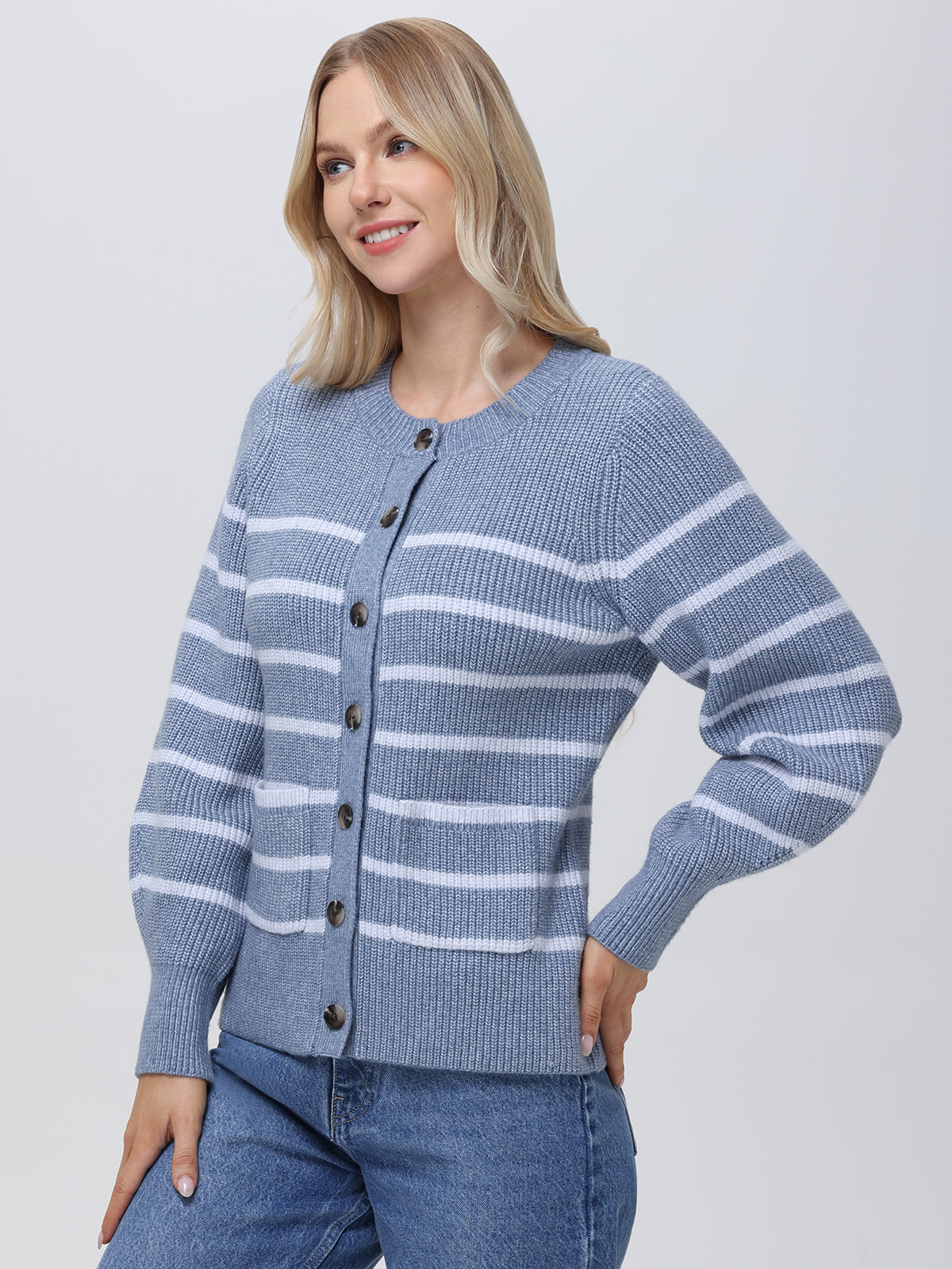 A person with long, light hair wears a 525 America blue and white striped cardigan featuring balloon sleeves, standing against a plain background in jeans. Their pose is relaxed, with one hand in a pocket.