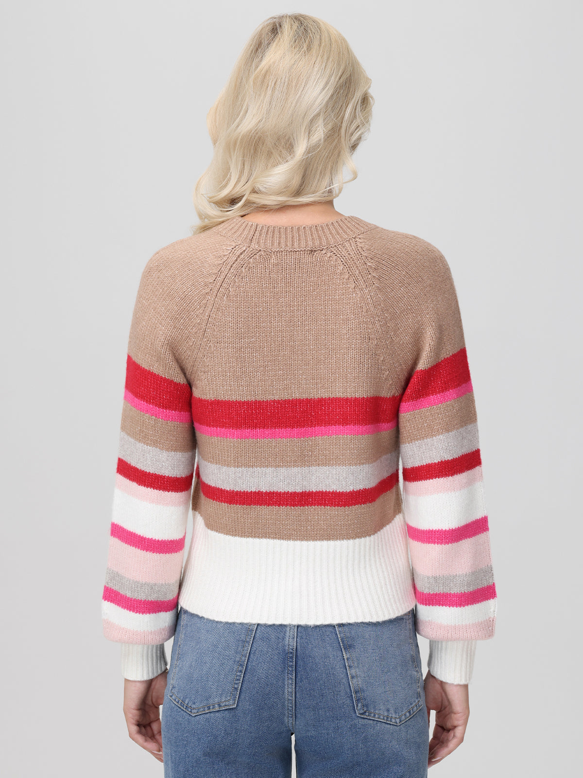 A person with long blonde hair wears a 525 America multicolored cropped pullover featuring colorblock stripes in brown, red, pink, gray, and white, paired with blue jeans. They stand with their back to the camera against a plain background.