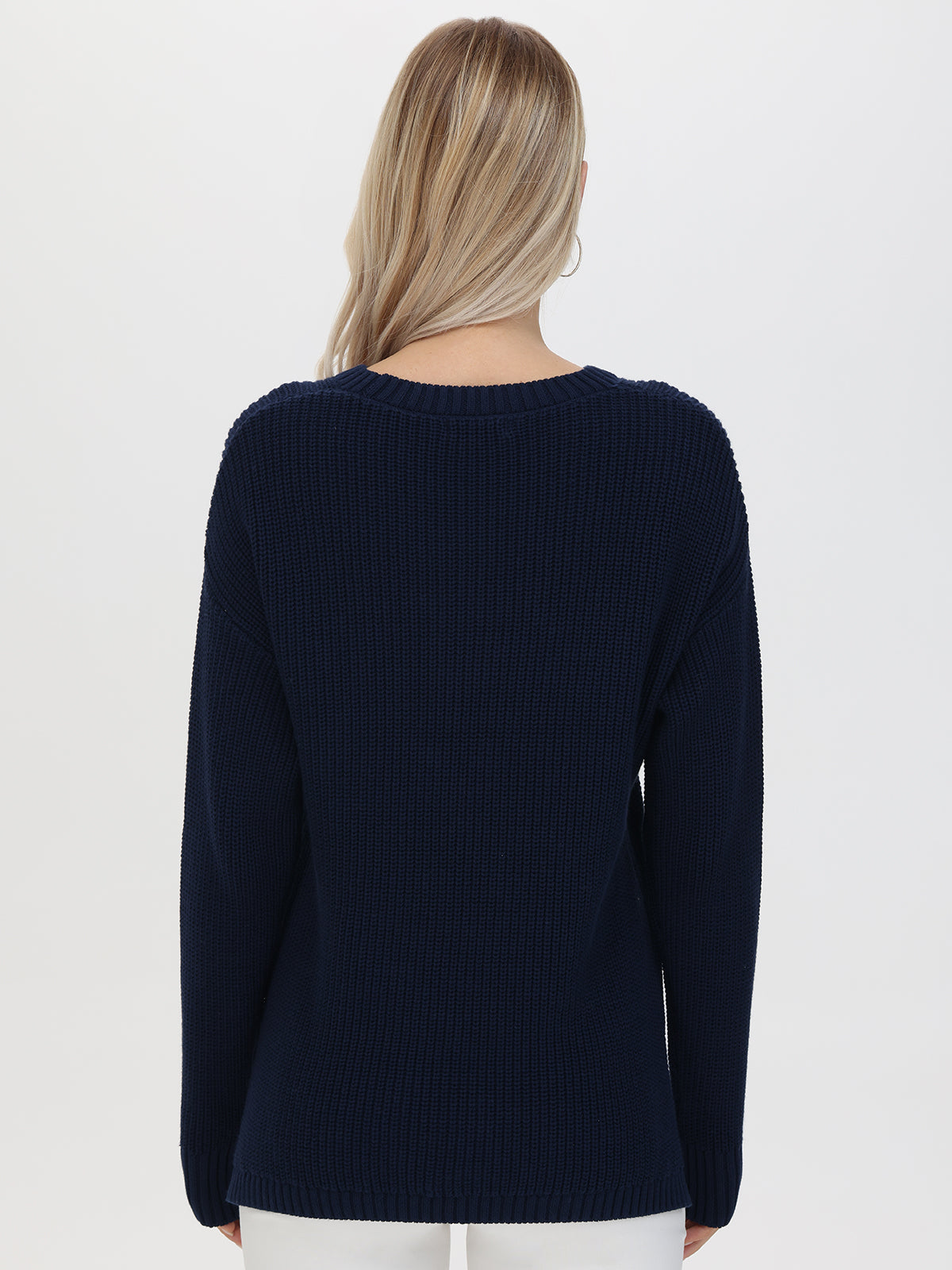 The image features a person with long blond hair in a relaxed-fit, dark blue 525 America Boston sweater. The high-low hem and simple design add to its casual elegance, as the individual stands against a plain white background.