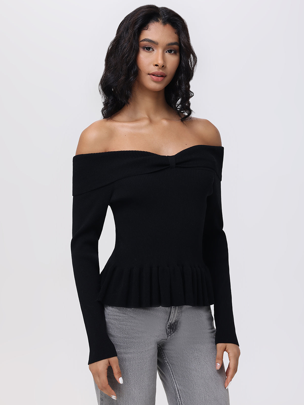 A person with long, dark hair is wearing a chic 525 America Off Shoulder Peplum Pullover with long sleeves and gray jeans, adding a versatile touch against the plain white background.