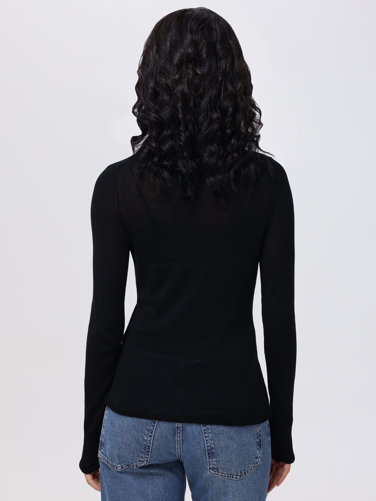 Rear view of someone with long, curly hair in a fitted black 525 America turtleneck and blue jeans against a plain white background.