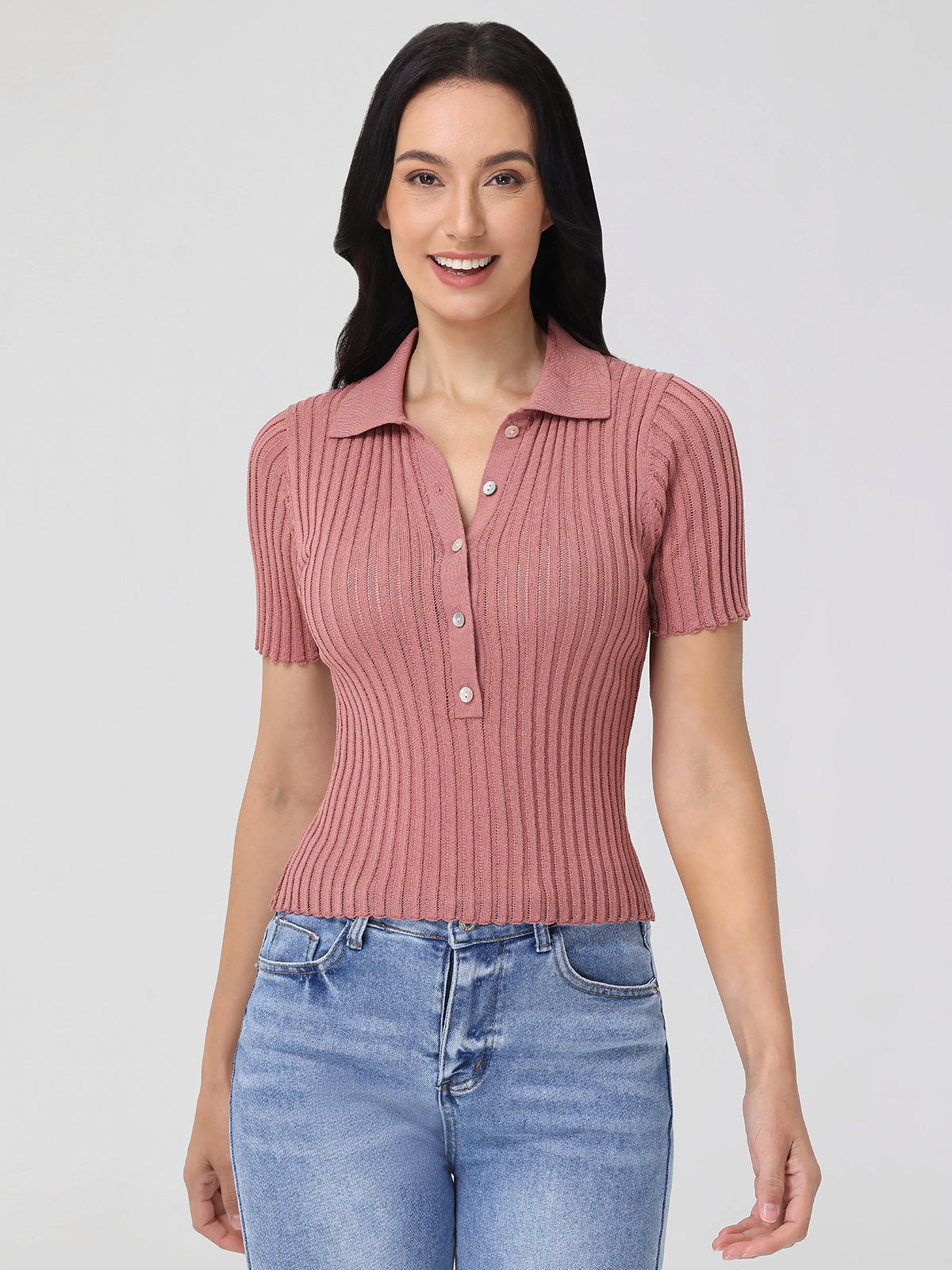 A person with long dark hair wears a ribbed, short-sleeve pink shirt by 525 America, with a statement neckline, and pairs it with blue jeans. Theyre set against a plain light gray background.