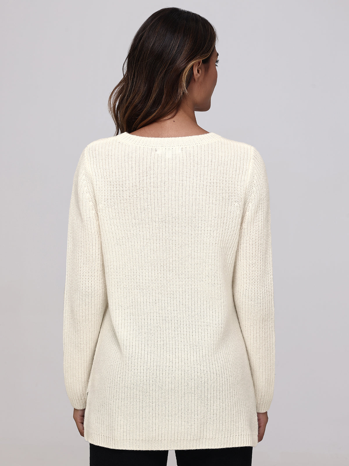 The image displays a person with long hair in a cream, relaxed-fit cashmere sweater by 525 America. The luxe piece has a simple, straight design with long sleeves. The backdrop is plain light gray.