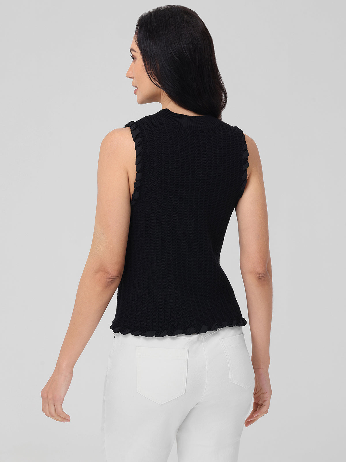 A person with long dark hair is seen from the back, wearing a 100% cotton fitted tank with frilled edges by 525 America, paired with white pants against a plain gray background.