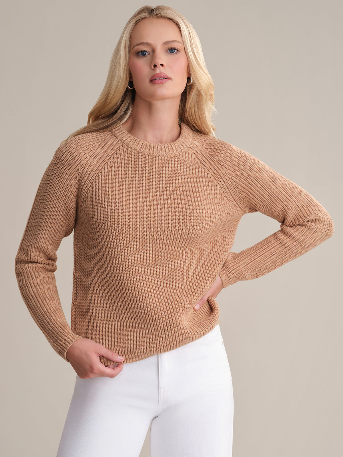 A person with long blonde hair is wearing the Jane: Crewneck Shaker Stitch Cotton Sweater and white pants, posing against a plain background. One hand rests on their waist while they maintain a neutral expression.